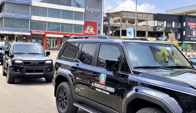 Black Toyota Prado SUVs, one branded "All Progressives Congress, Government House Abuja", parked on a street in Abuja
