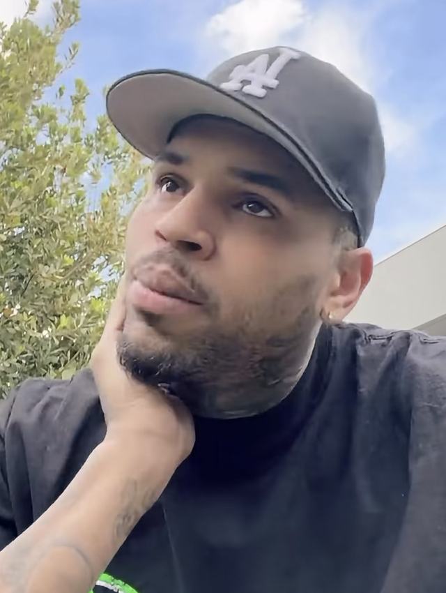 Chris Brown in a black cap, resting his chin on his hand