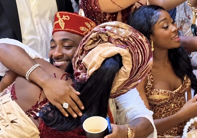Davido, in a red cap, smiles as he hugs a guest in a gele at Zlatan Ibile's wedding