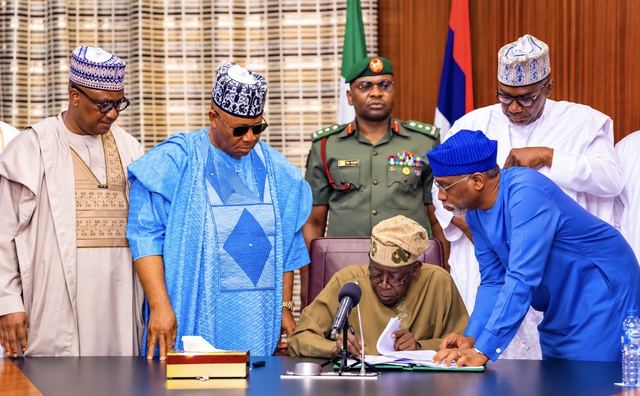 President Bola Tinubu signs a document at a table as Vice President Kashim Shettima and other officials look on
