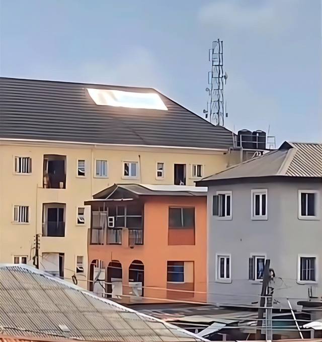 Sunlight glares off solar panels on the dark roof of a cream three-storey building, seen from a neighbouring rooftop