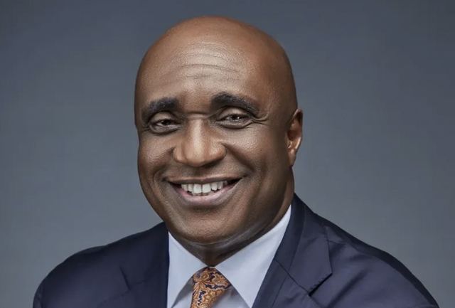 Pastor David Ibiyeomie smiling in a navy suit and patterned tie against a grey background
