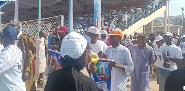 Crowds in party caps and T-shirts, some holding APC posters, arrive at a stadium in Kaduna